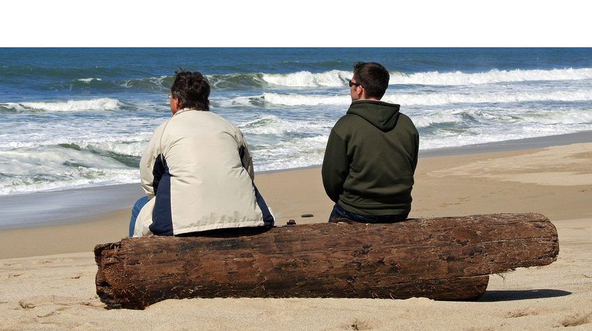 Two men sitting at the beach and talking