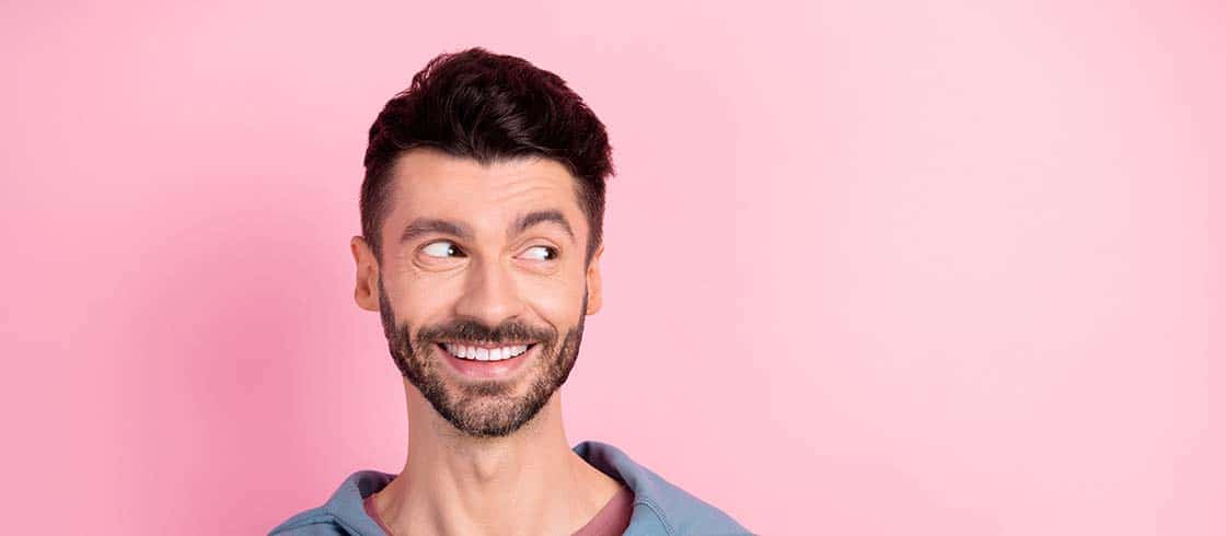 Photo of dreamy charming young happy man look empty space good mood isolated on pink color background.