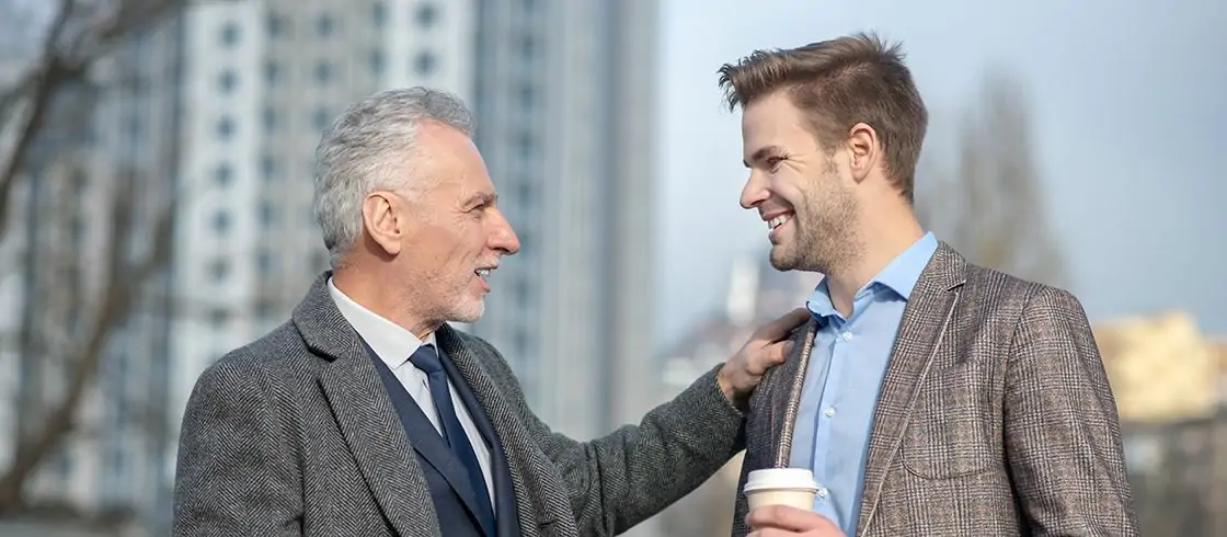 Friends. Young businessman and his mature mentor smiling while having a conversation